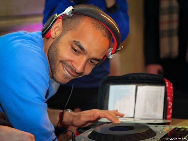 DJ Mehdi souriant, casque sur les oreilles, devant une platine