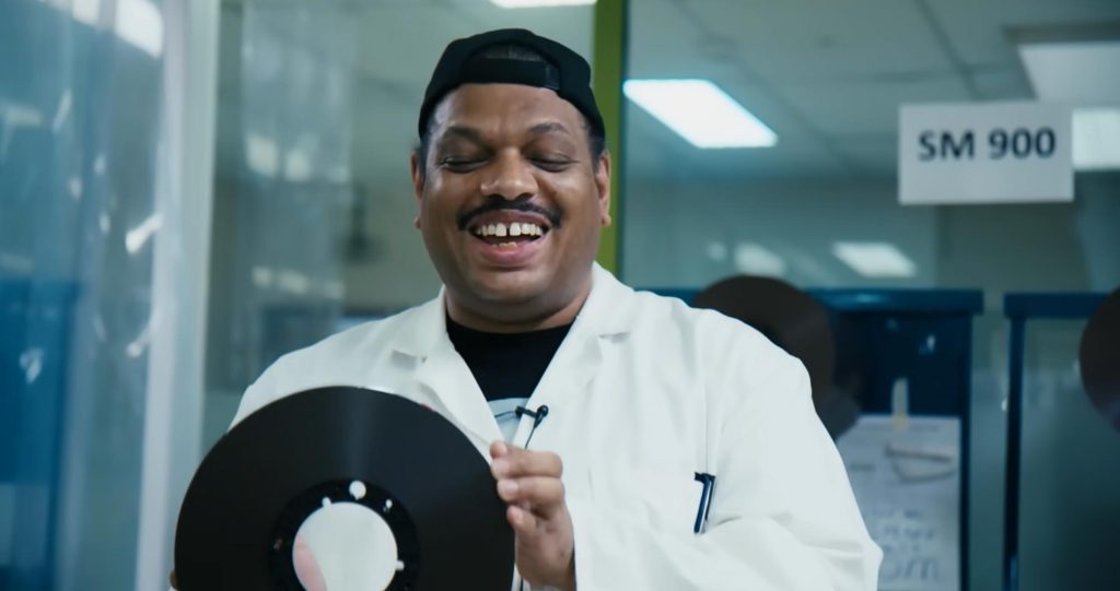 Kerri Chandler souriant et tenant une bande de magnétophone dans un laboratoire