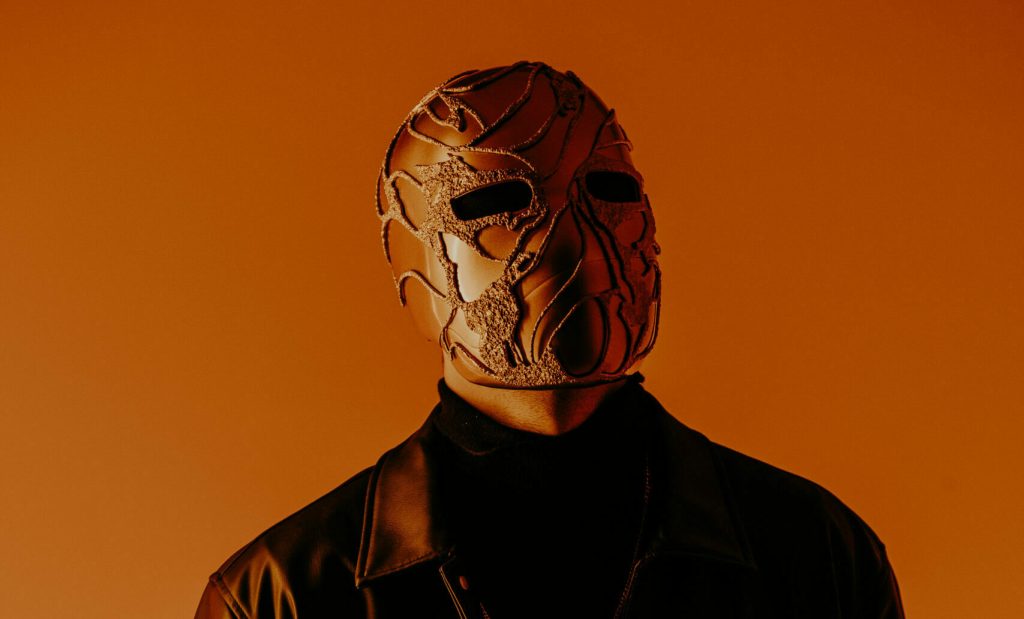 Mr Tout le Monde portant son masque sculpte sur fond orange